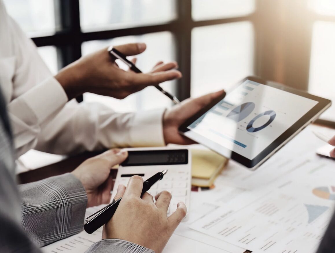 Two people looking at graphs and using a calculator. People reviewing financial graphs and using a calculator during a business analysis.